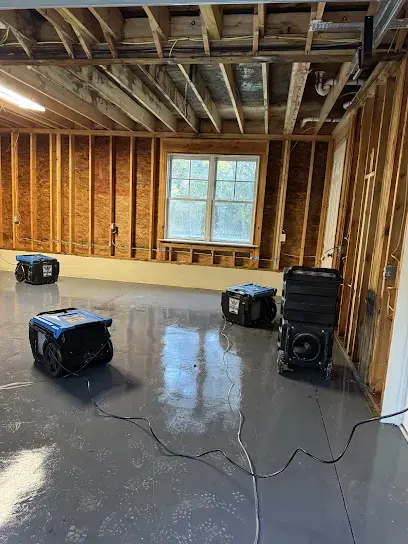 Gutted room with dehumidifiers running on a wet concrete floor