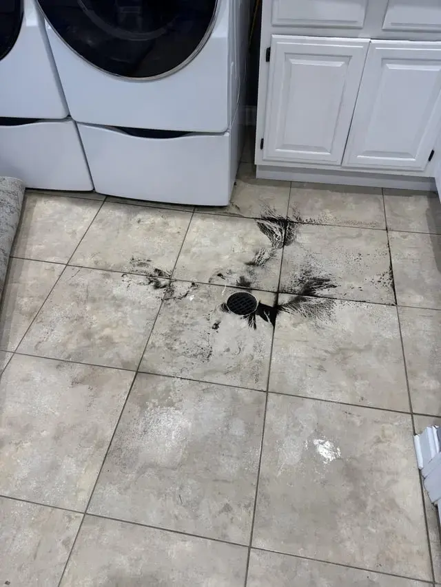 Water leaking across a laundry room tile floor beside the washer